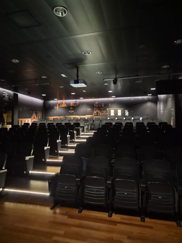 Collegezaal van Inholland met zicht op het podium en presentatiescherm.